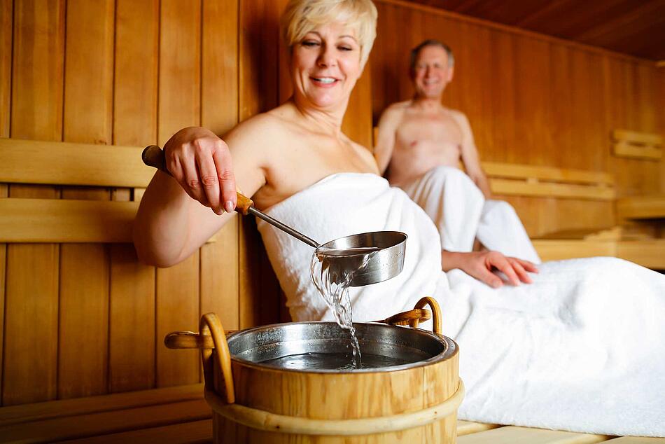 Paar in der Sauna, die Frau macht einen Aufguss