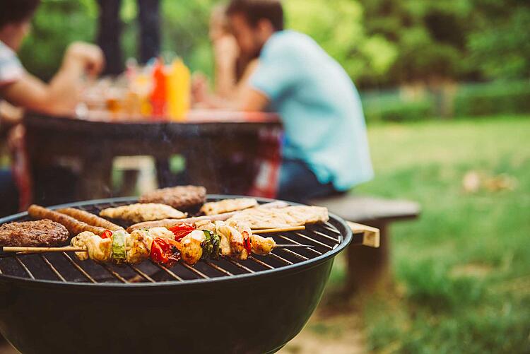 Grill im Vordergrund, dahinter Gruppe beim Essen