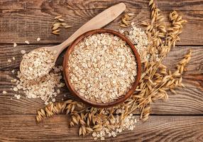 Haferflocken in einer Schüssel und auf einem Holzloeffel daneben Haferähren