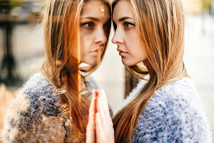 Frau lehnt Stirn und Hände an einen Spiegel