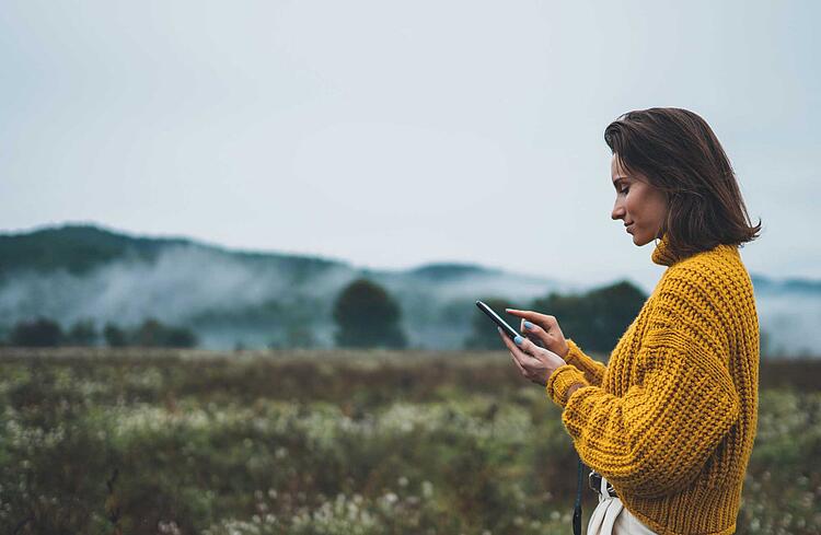 Frau in der Natur schaut auf ihr Smartphone