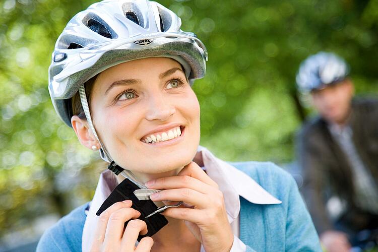 Junge Frau zieht sich einen Fahrrhelm an.