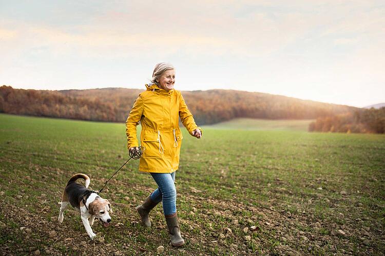 Ältere Frau macht einen Spaziergang mit ihrem Hund in herbstlicher Natur.