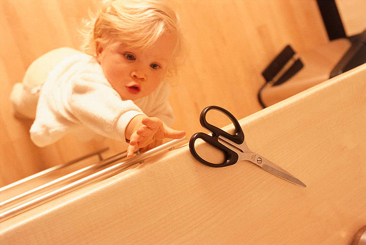 Kleinkind streckt sich nach einer Schere auf einer Arbeitsplatte. - Bildnachweis: © wdv / Jan Lauer Kleinkind streckt sich nach einer Schere auf einer Arbeitsplatte.