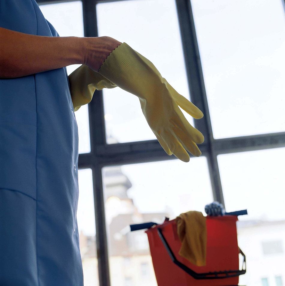 Frau mit Kittelschürze zieht sich Gummihandschuhe an. - Bildnachweis: © wdv / Günther Pfannmüller Frau mit Kittelschürze zieht sich Gummihandschuhe an.