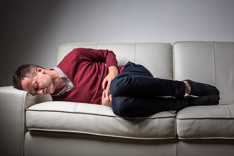 Mann liegt mit Bauchschmerzen auf dem Sofa