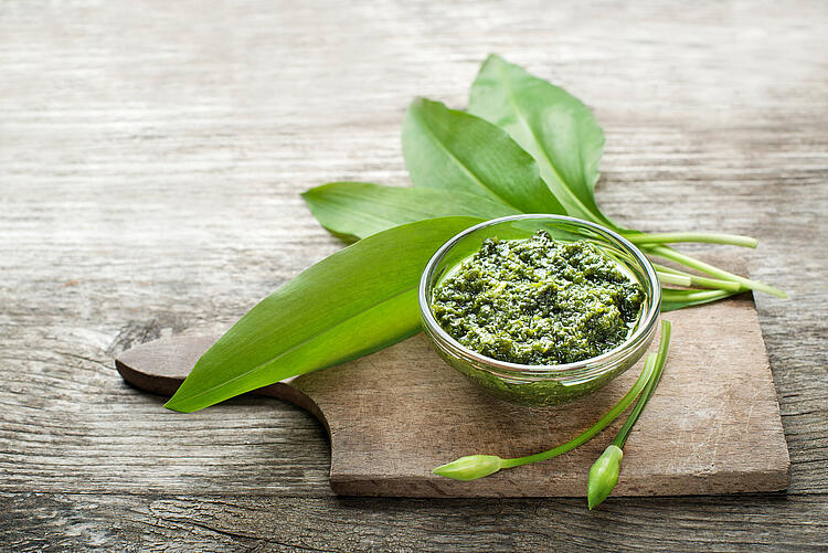 Bärlauchpesto in einer Glasschale daneben Bärlauchblätter und -blüten.