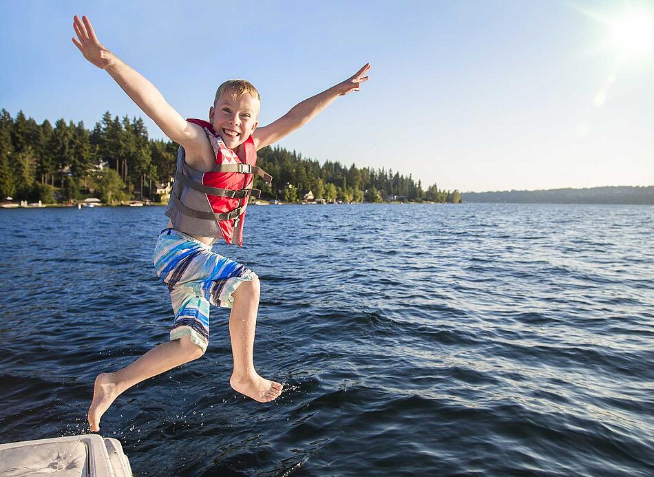 Junge mit Schwimmweste springt in einen See