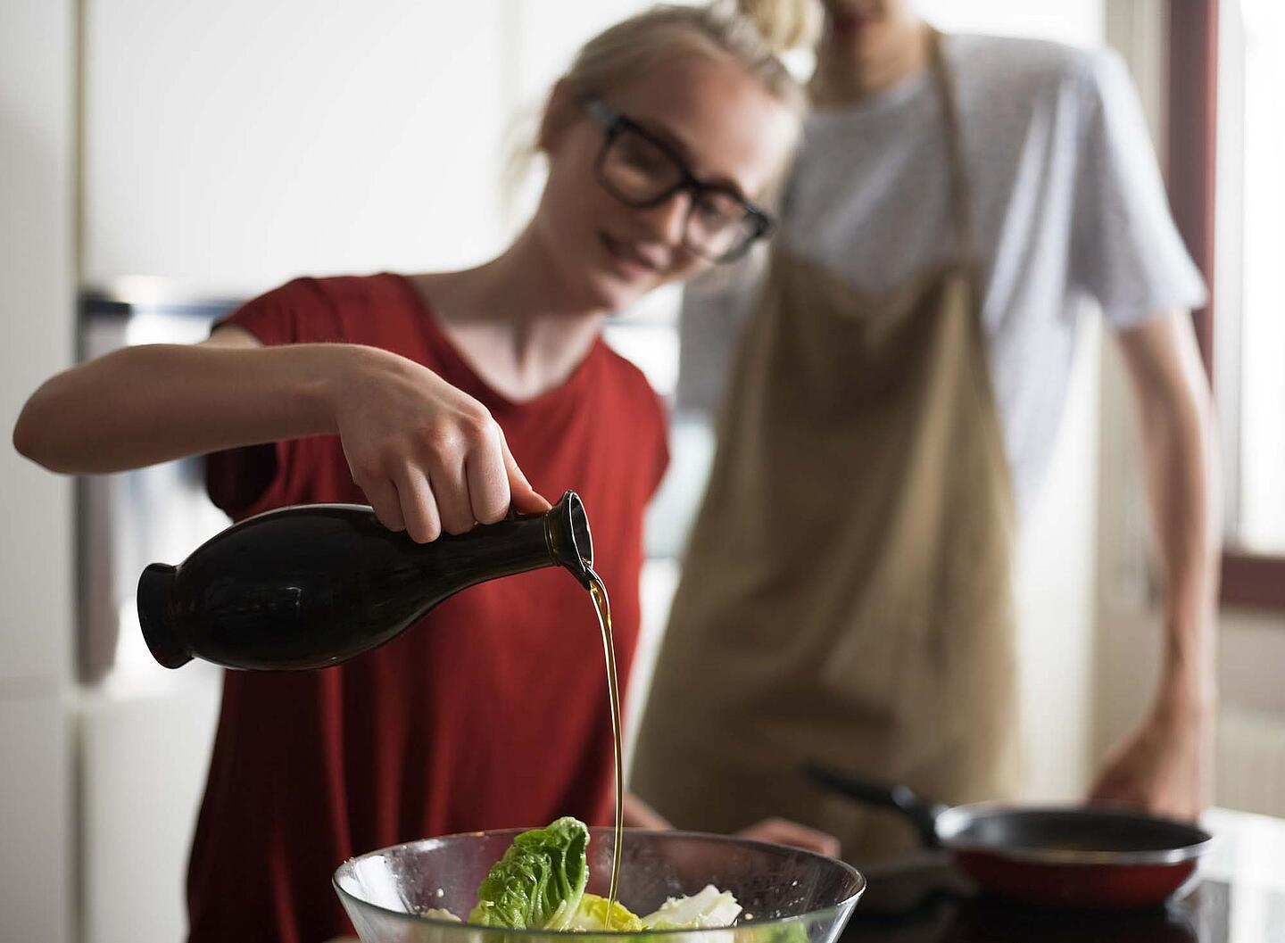 Eine Frau giesst Öl aus einer Karaffe in eine Schüssel mit Salat.