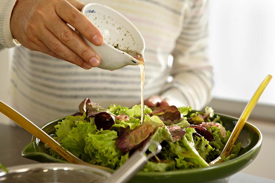 Männerhand schüttet Dressing über einen grünen Salat.