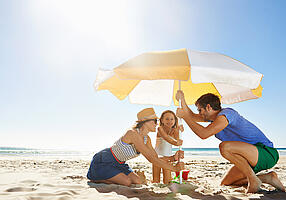 Familie stellt am Strand einen Sonnenschirm auf