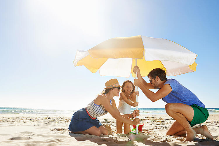 Familie stellt am Strand einen Sonnenschirm auf