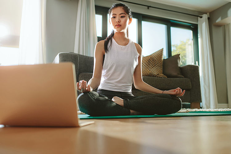 Bildnachweis: © stock.adobe.com/ / Jacob Lund Eine Frau macht eine Yogaübung und schaut dabei auf ihren Laptop.