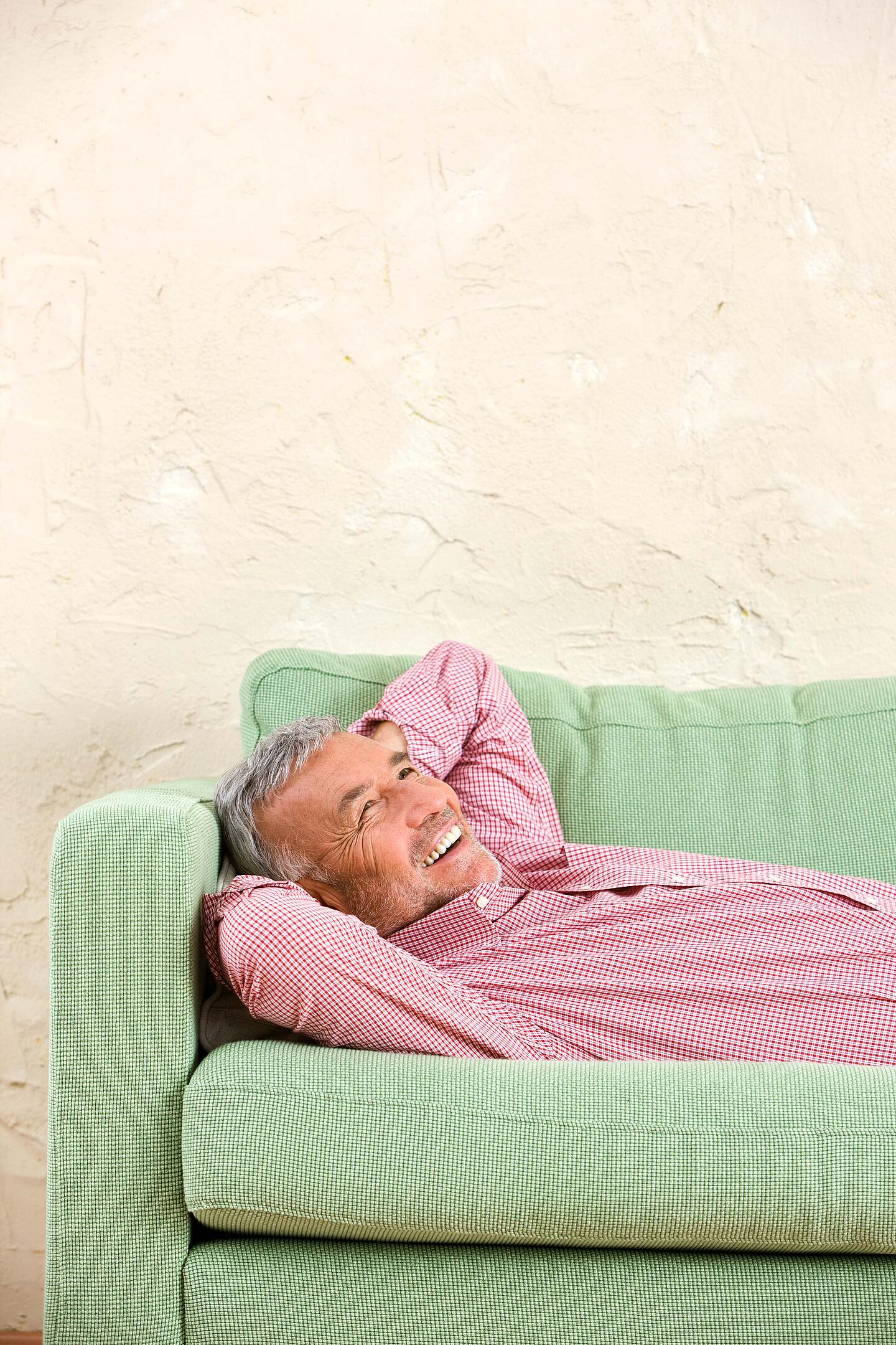 Ein Mann liegt mit hinter dem Kopf verschränkten Armen auf einem grünen Sofa.