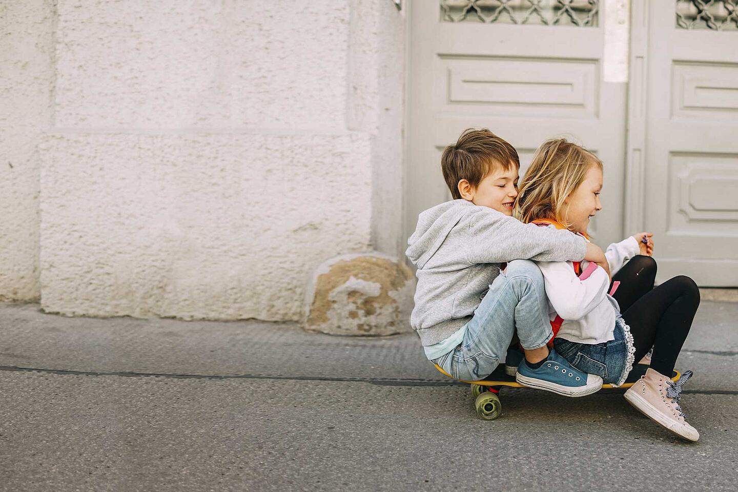 Ein Junge und ein Mädchen sitzen zusammen auf einem Skateboard