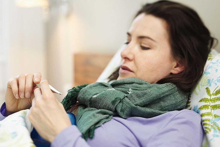 Frau mit Fieberthermometer in der Hand.