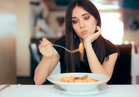 Frau schaut unglücklich auf einen Teller Pasta