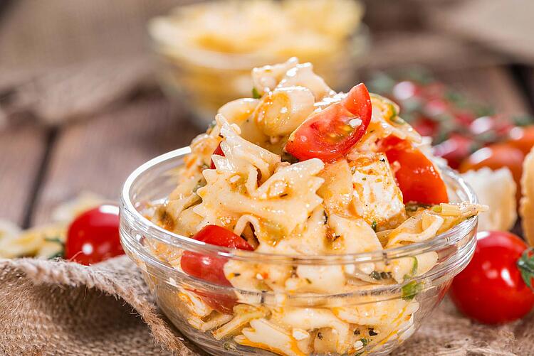 Nudelsalat mit frischen Tomaten in einer Glasschüssel.