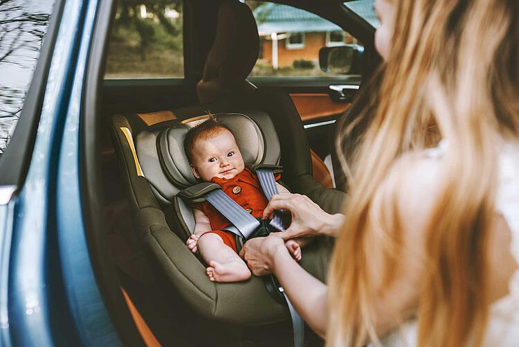 Mutter schnallt ihr Baby im Kindersitz im Auto an