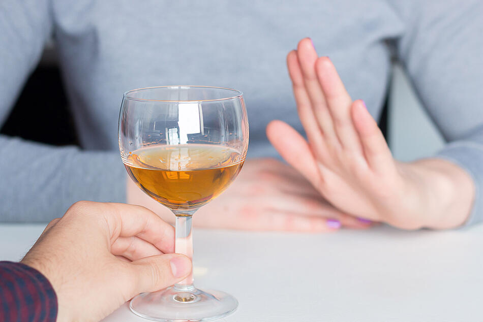 Mann bietet einer Frau ein Glas Wein an, die Frau macht eine abwehrende Handbewegung.