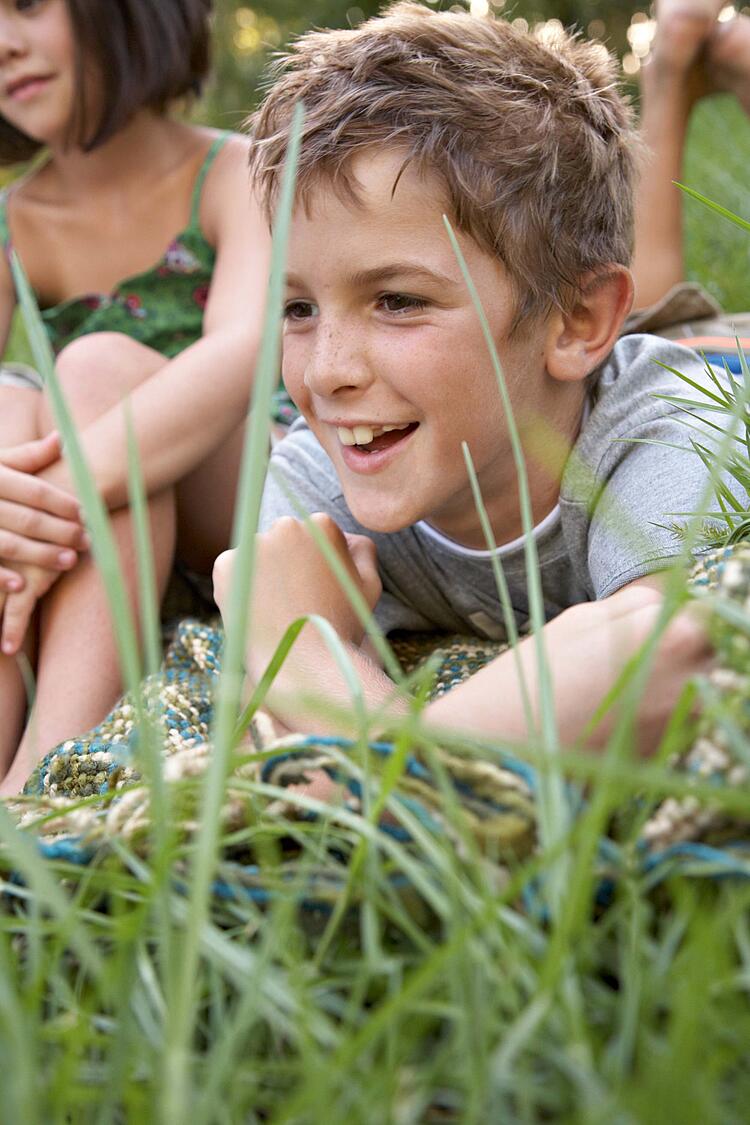 Zwei Kinder auf einer Decke im Gras.