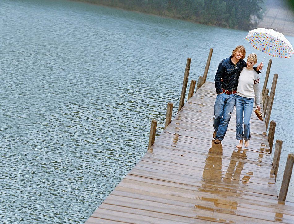 Ein paar läuft bei Regen über einen Steg am See. - Bildnachweis: © wdv / Günther Bauer Ein paar läuft bei Regen über einen Steg am See.