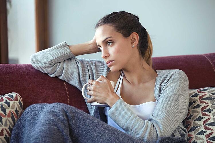 / nenetus Depressiv wirkende Frau sitzt nachdenklich auf der Couch.