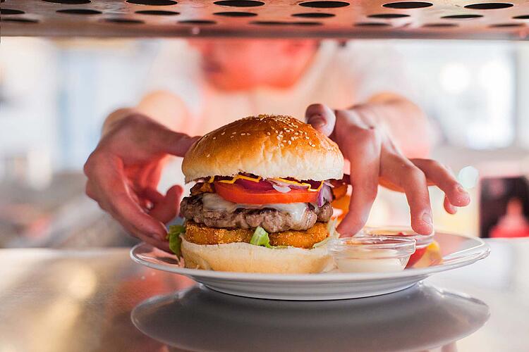 Hände legen einen Hamburger auf einen Teller.