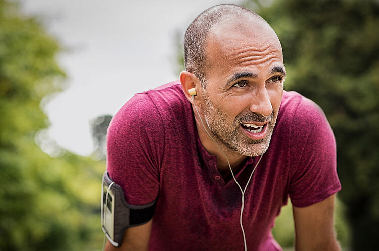 Mann macht Pause beim Joggen und stützt die Hände auf die Beine.