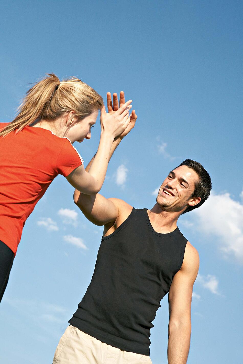 Frau und Mann in Sportkleidung vor einem blauen Himmel beim High-Five-Abklatschen.