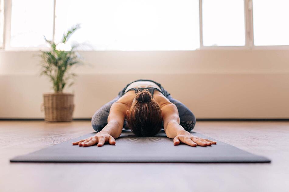 Eine Frau kniet auf einer Yogamatte, streckt beide Hände weit nach vorne und dehnt so ihre Brustmuskulatur.