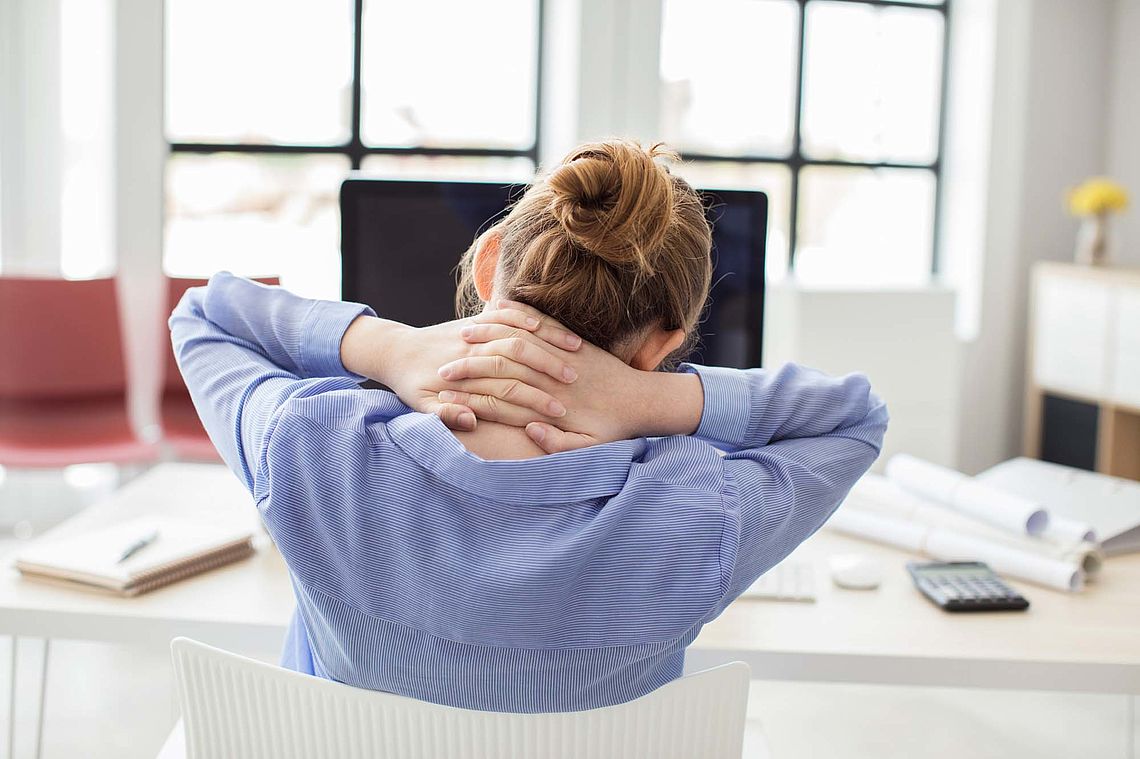 Junge Frau sitzt an einem Schreibtisch und verschränkt die Hände im Nacken, Ansicht von hinten. – Bild: istockphoto.com /seb_ra - Bildnachweis: © istockphoto.com / seb_ra Junge Frau sitzt an einem Schreibtisch und verschränkt die Hände im Nacken, Ansicht von hinten.