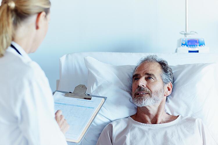 Mann in Krankenhausbett wird von Ärztin befragt