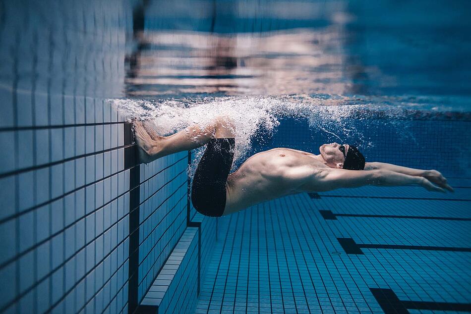 Ein Mann stößt sich beim Schwimmen vom Beckenrand ab.