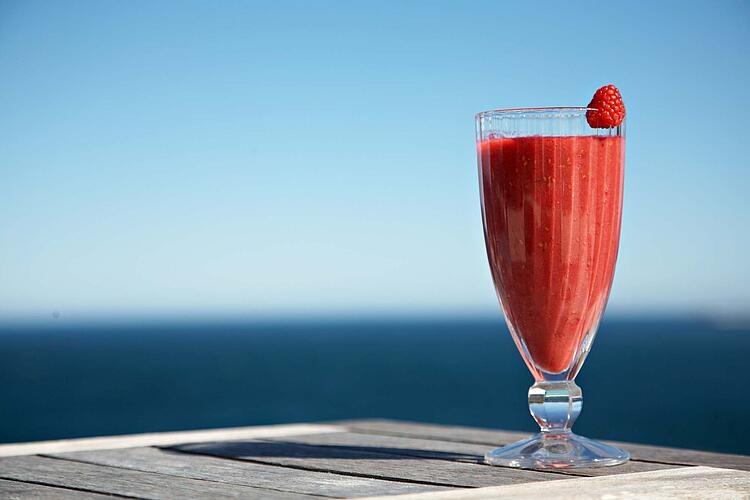 Ein Glas Himbeersmoothie, im Hintergrund blauer Himmel.