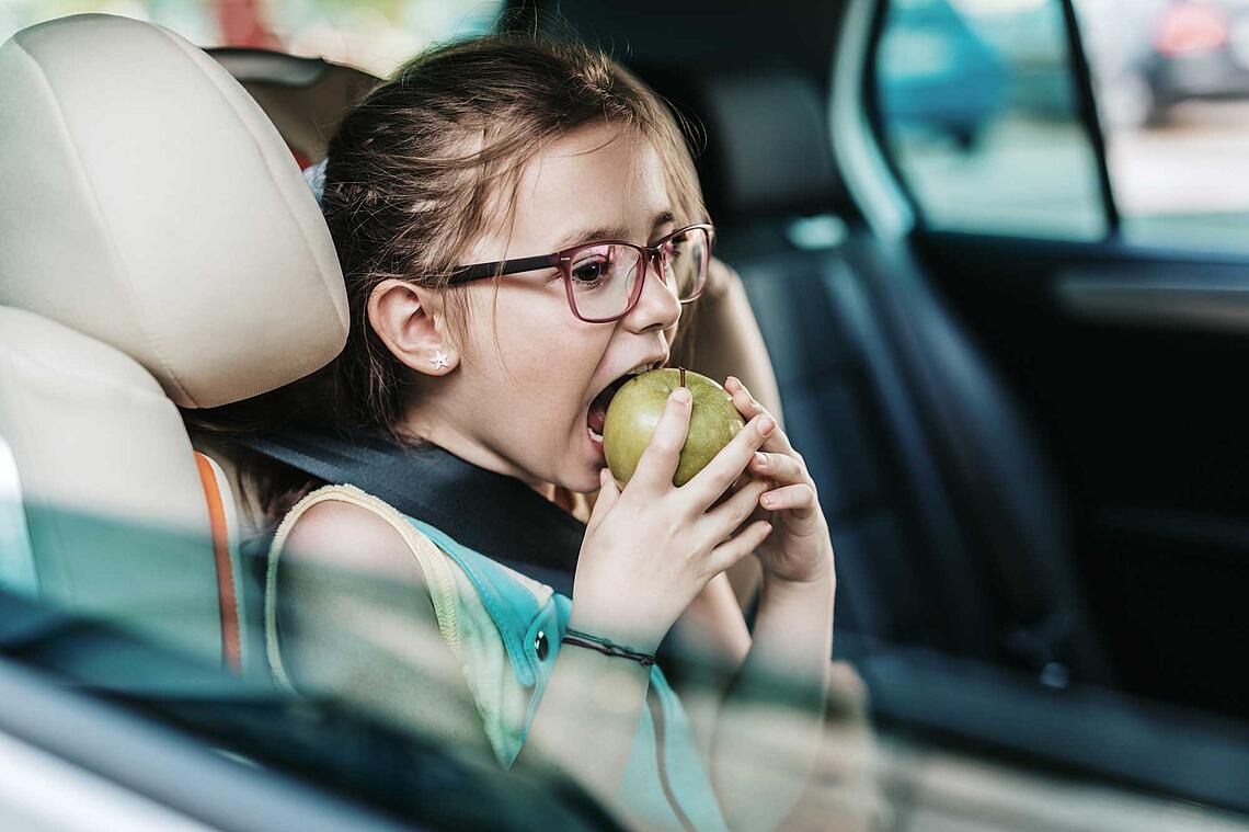 Mädchen im Kindersitz im Auto beisst in einen Apfel