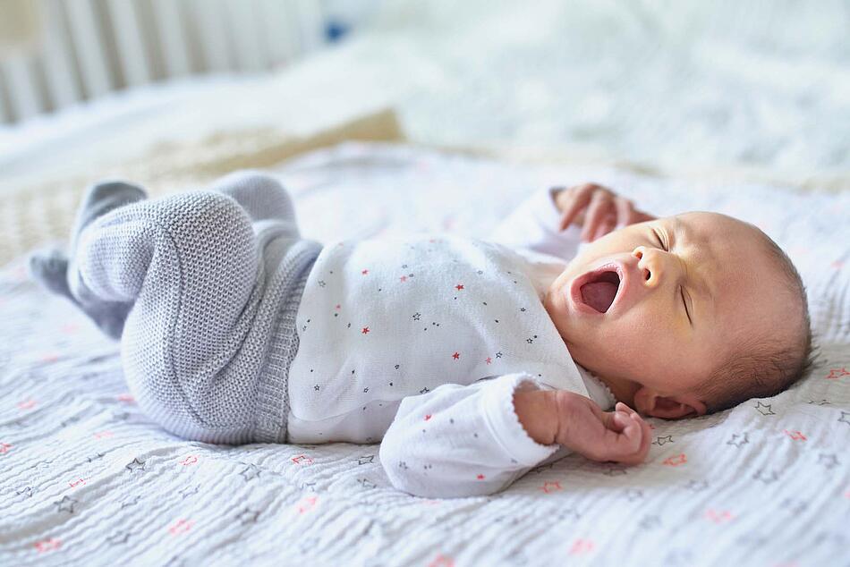 Ein Säugling liegt gähnend auf einer Decke - Bildnachweis: © stock.adobe.com / Ekaterina Pokrovsky Ein Säugling liegt gähnend auf einer Decke