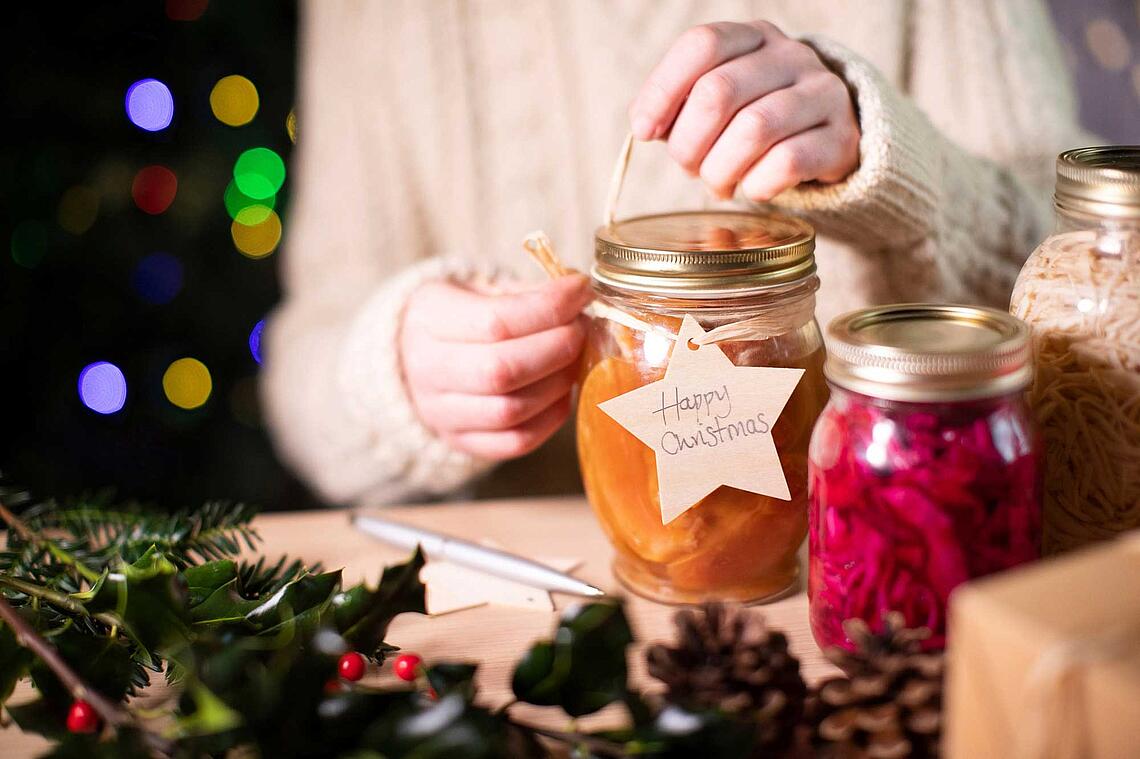 Hände versehen Eingemachtes mit einem Geschenkanhänger