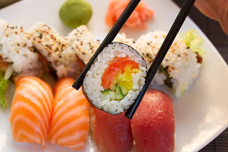 Essstäbchen halten ein Stück Sushi über einem Teller mit verschiedenen Sushi-Sorten.