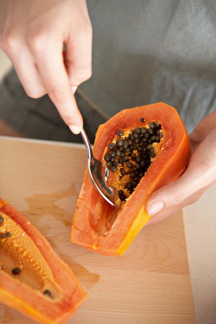 Frauenhände entkernen mit einem Löffel eine Papaya.