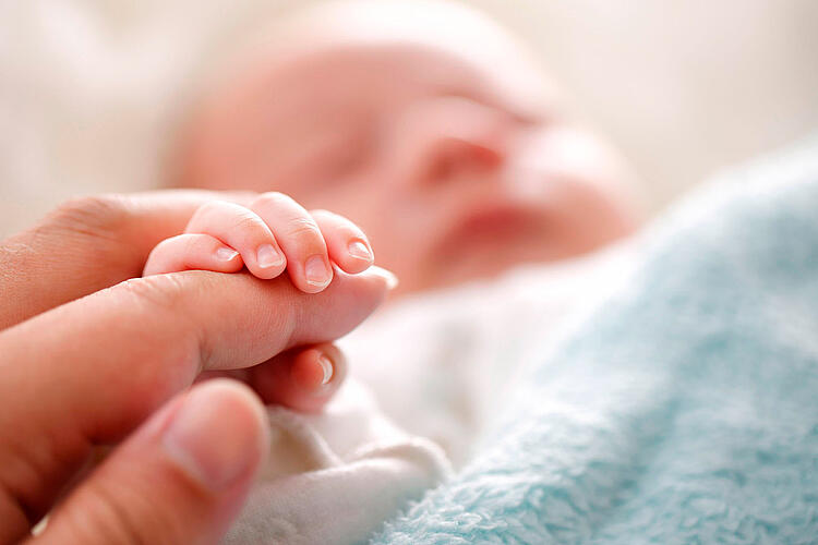 Baby umfasst mit der Hand einen Finger der Mutter.