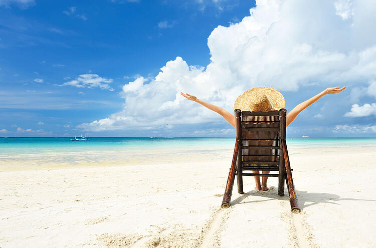 Frau mit Strohhut sitzt am Strand in einem Stuhl.