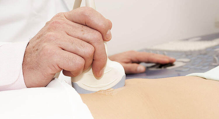 Hand eines Arztes macht einen Ultraschall vom Bauch einer Patientin.