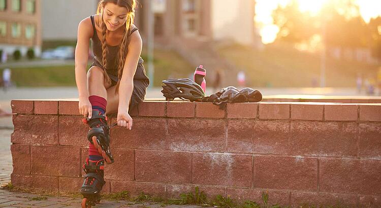 Bildnachweis: © istockphoto.com / AZImages Frau zieht sich auf einer Mauer sitzend ihre Inline Skates an.