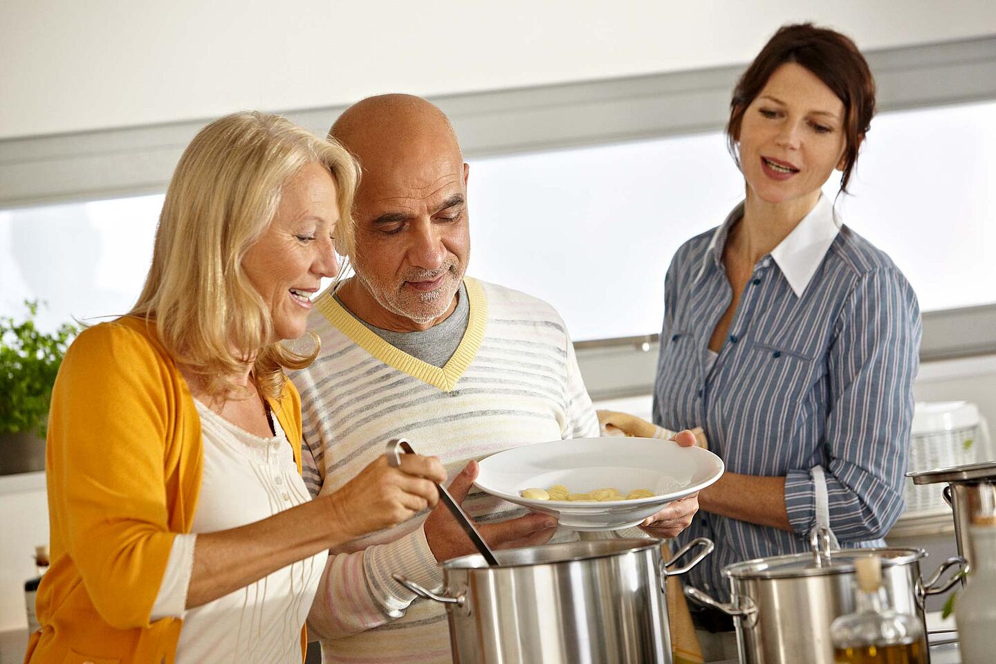 Zwei Frauen und ein Mann beim Kochen.