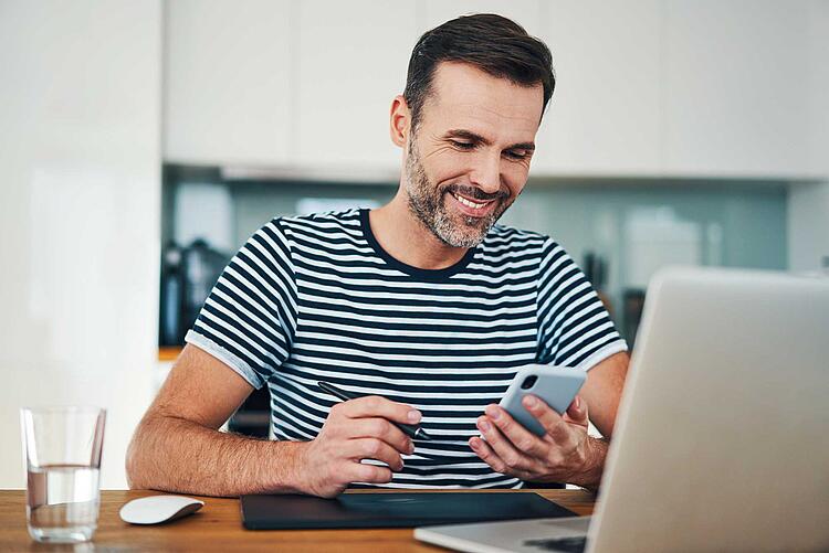 Mann mit Smartphone in der Hand sitzt am Laptop.