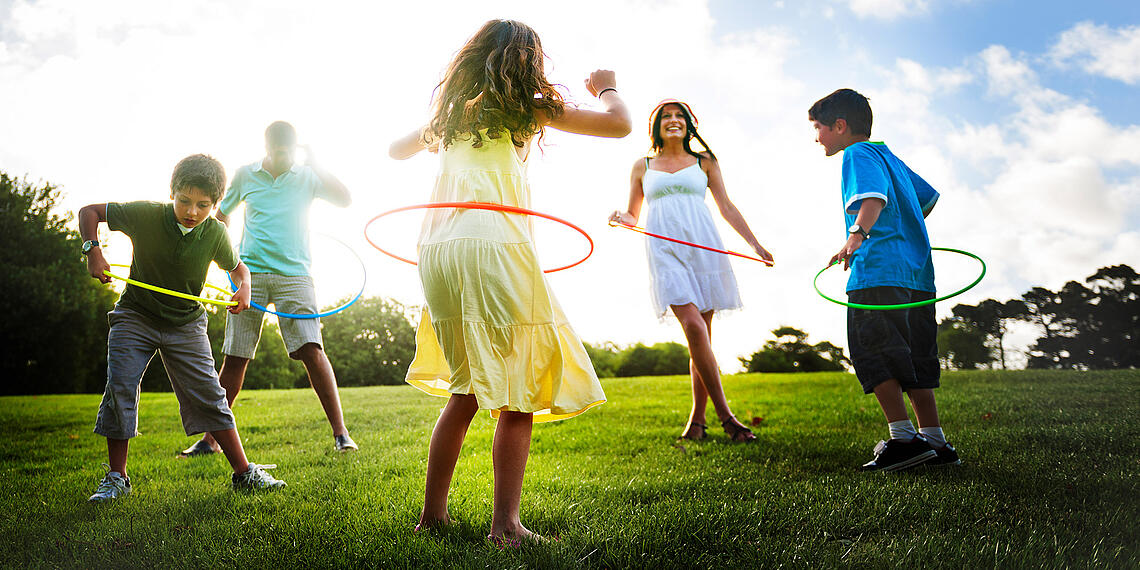 Die ganze Familie spielt Hula Hoop auf einer Wiese