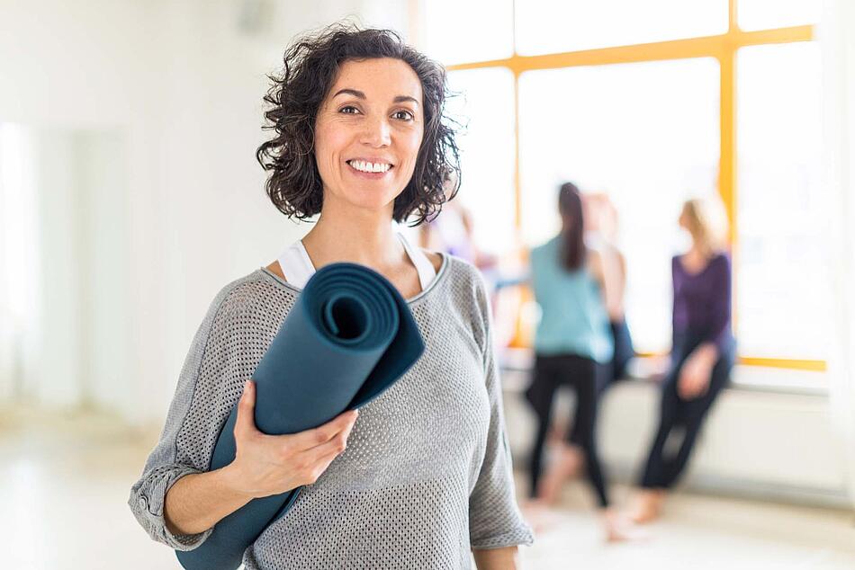 Eine Frau im Studio mit einer Yogamatte unter dem Arm.