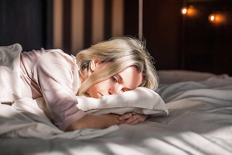 Traurige Frau liegt im Bett und umarmt ihr Kopfkissen