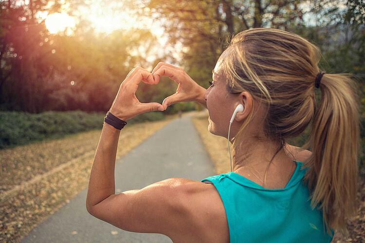 Frau joggt im Park und formt mit den Händen ein Herz.